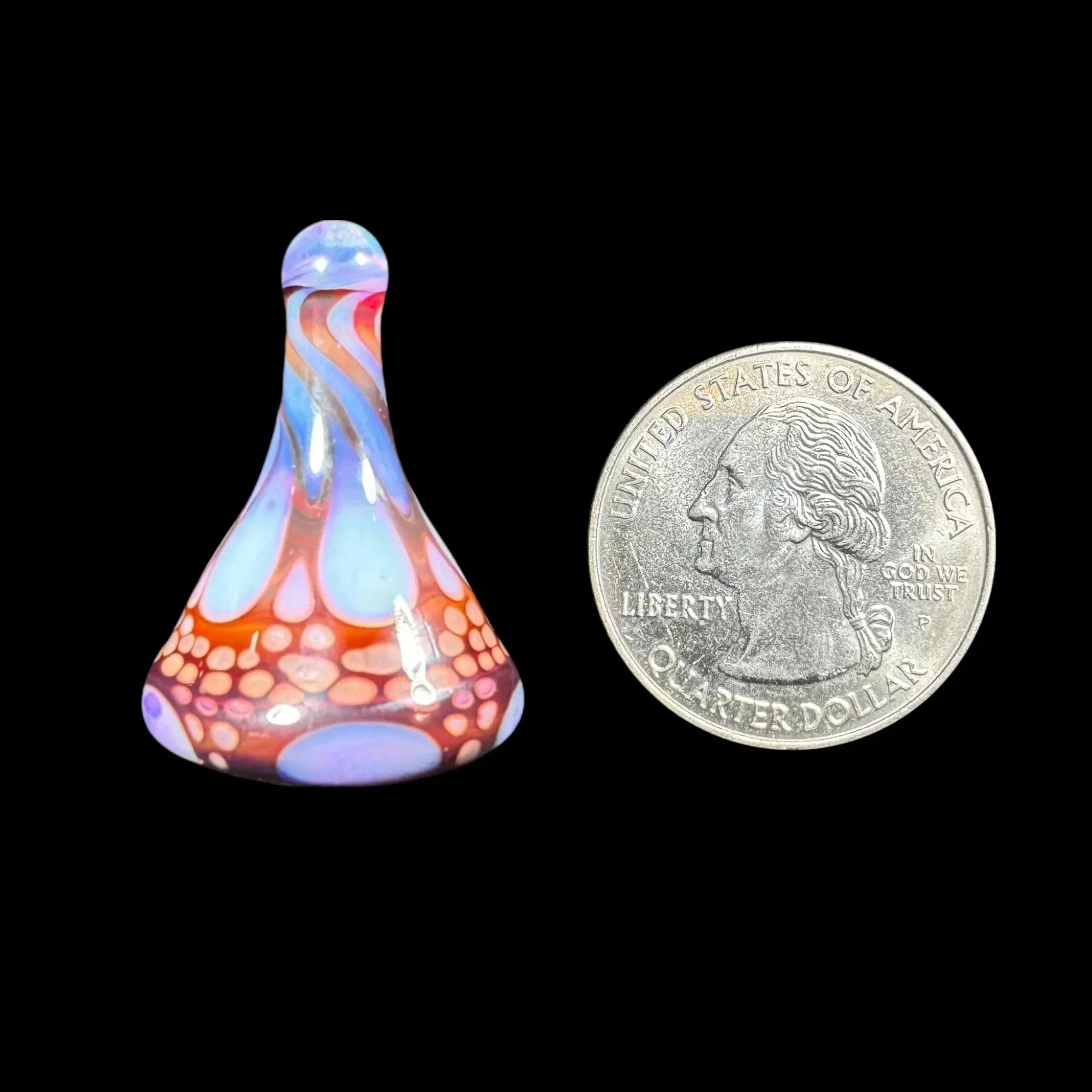 Colorful glass carb cap with swirling patterns next to a US quarter on black background