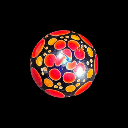 Handcrafted glass marble with red and orange bubble patterns on a dark background