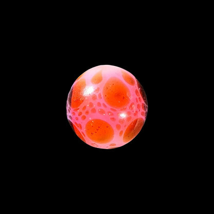 Handcrafted glass marble with pink and orange bubble pattern on black background
