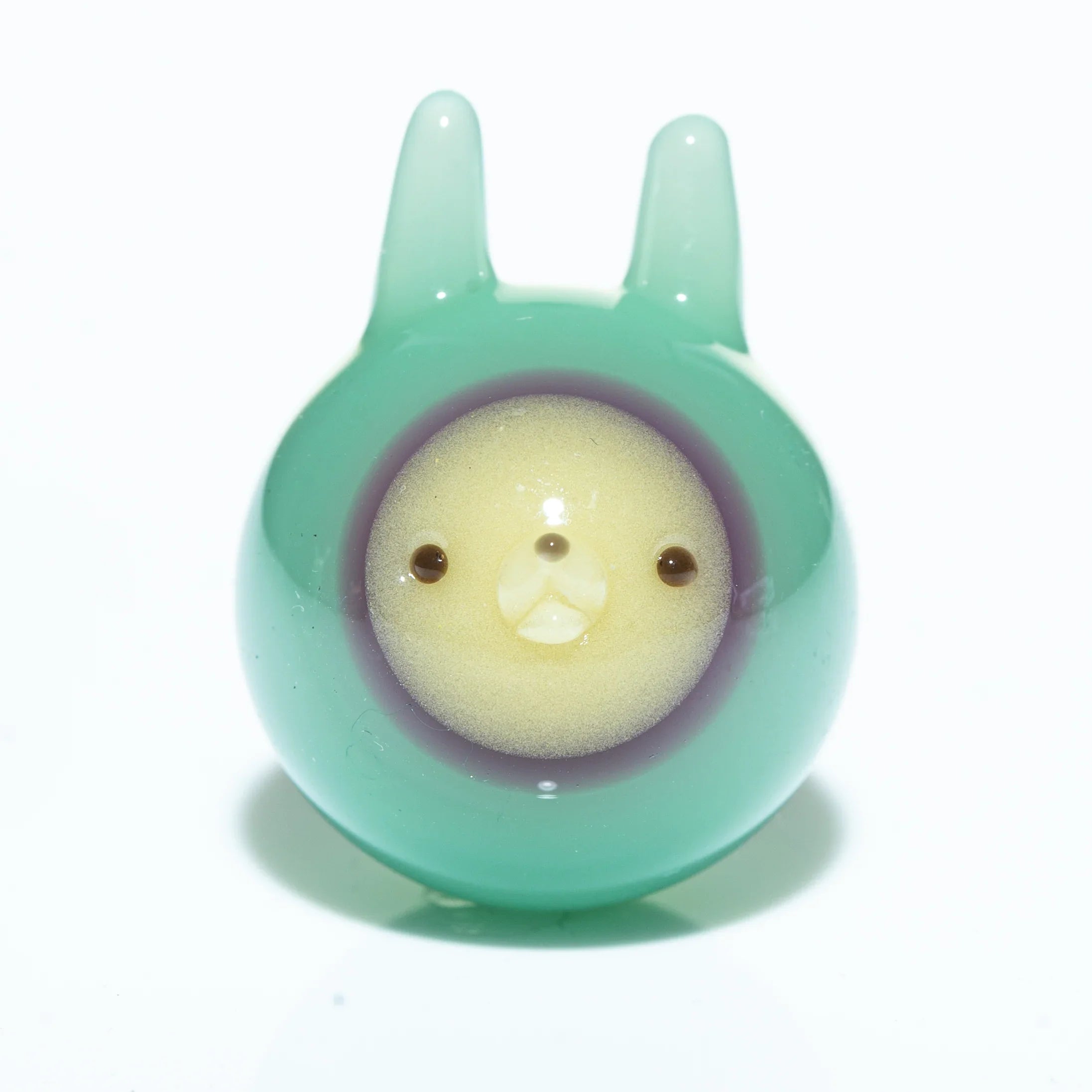 Seafoam green glass marble with cute animal face and ear-like details, white background