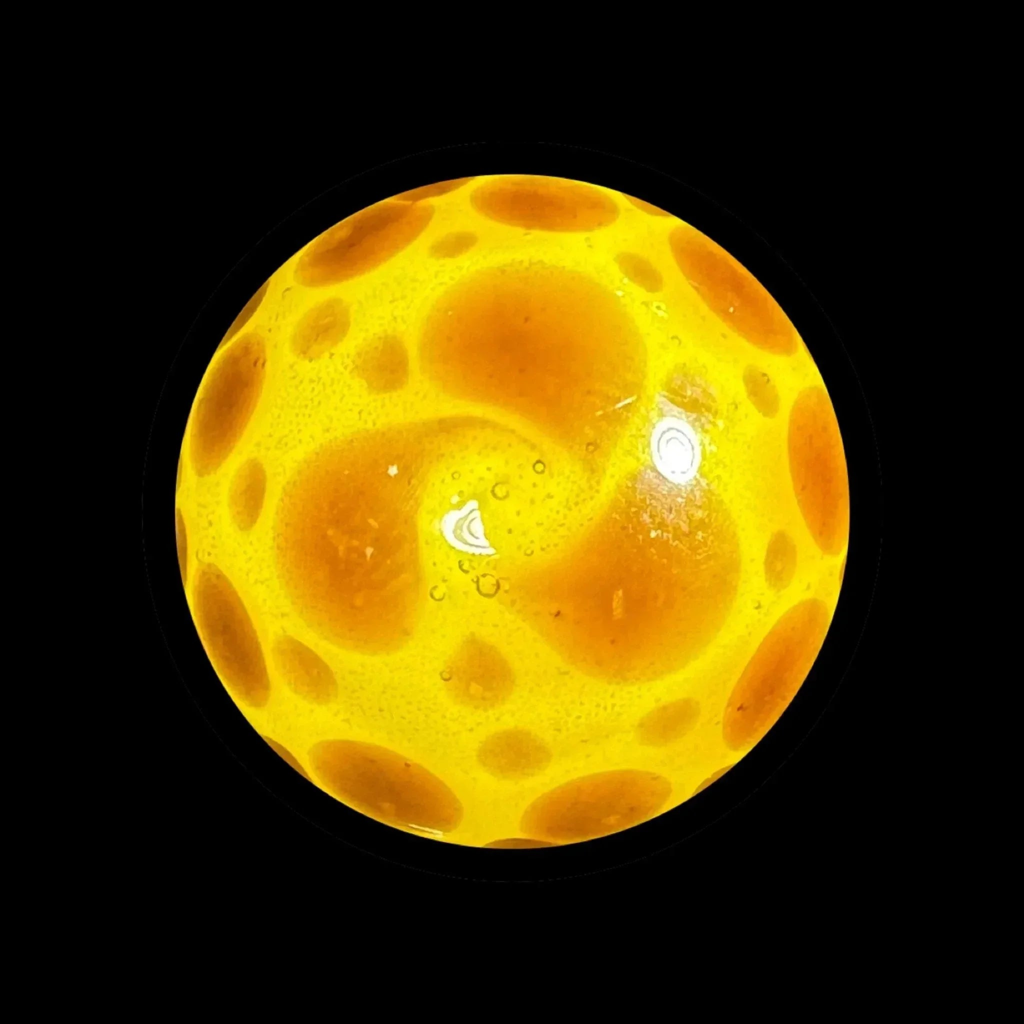Yellow glass marble with orange bubble patterns on black background