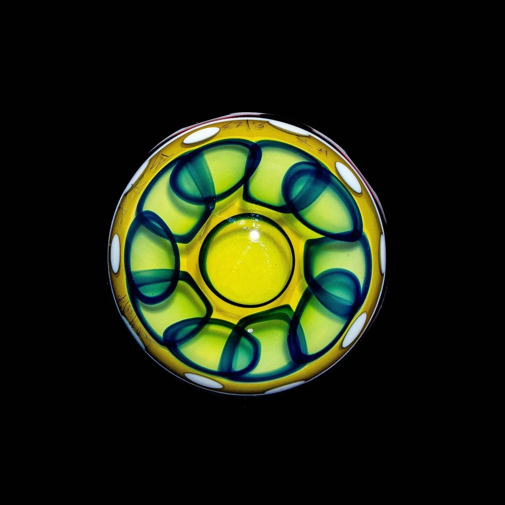 Colorful glass bowl with yellow and green swirled design and white accents on black background.
