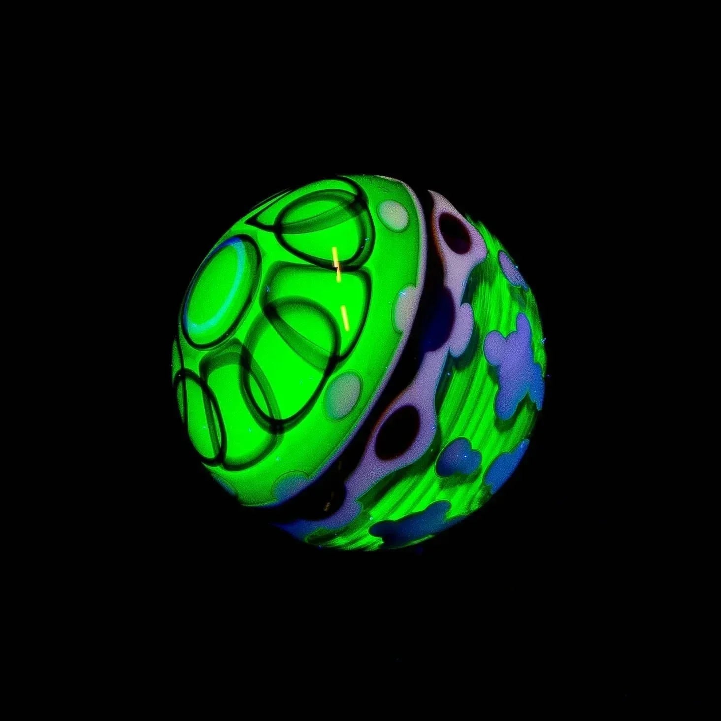 Glowing glass marble with green, purple, and blue patterns on black background