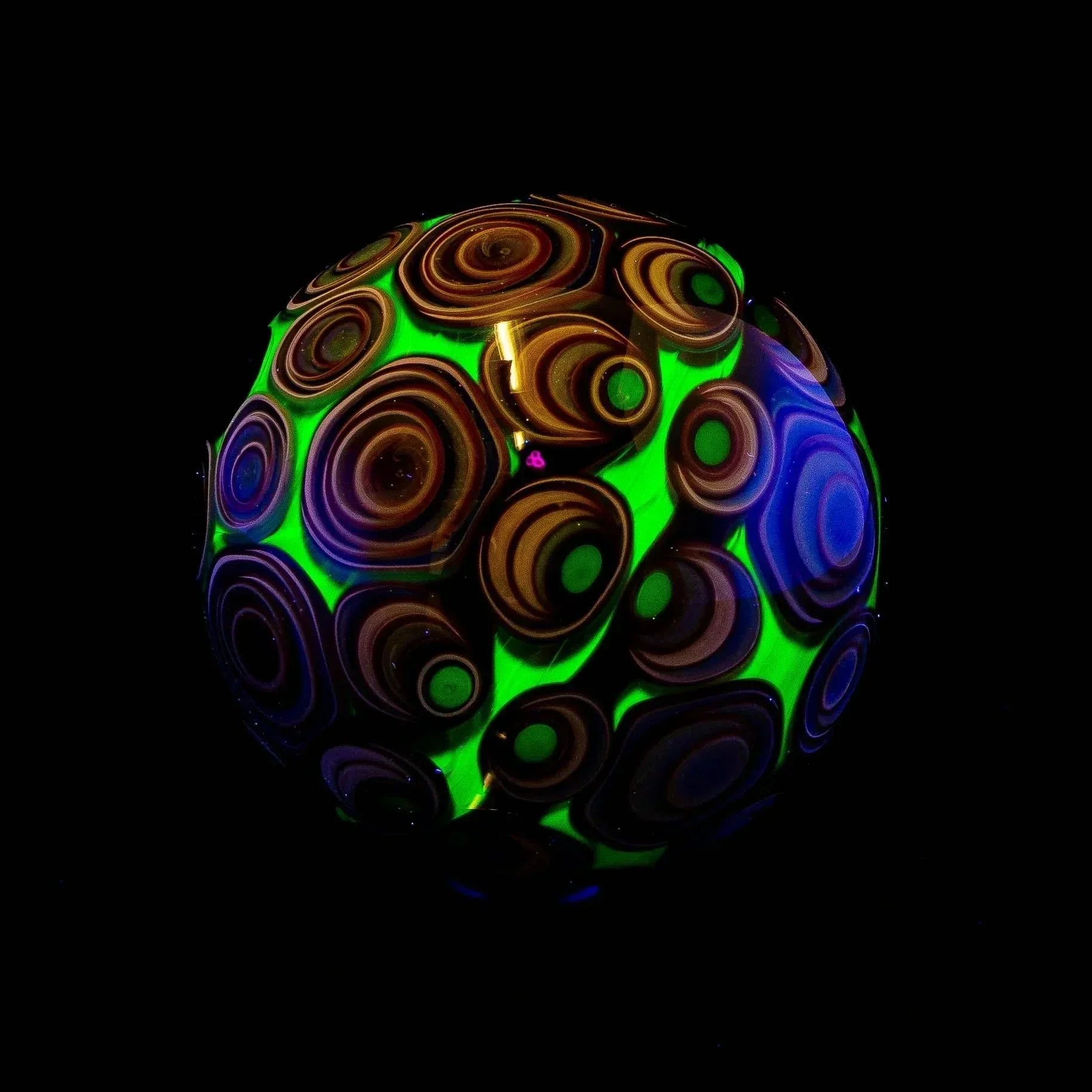 Handmade glass marble with neon UV reactive swirls and vortex pattern on a black background