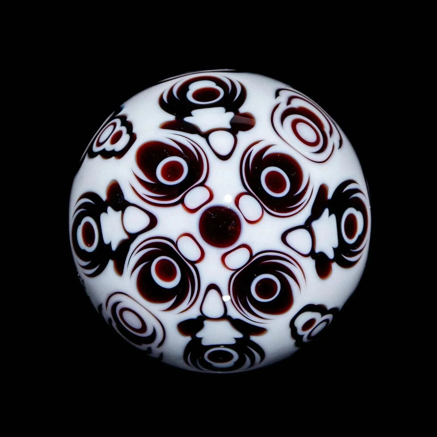 Intricate white glass marble with black and red geometric patterns on a black background.