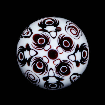Intricate white glass marble with black and red geometric patterns on a black background.