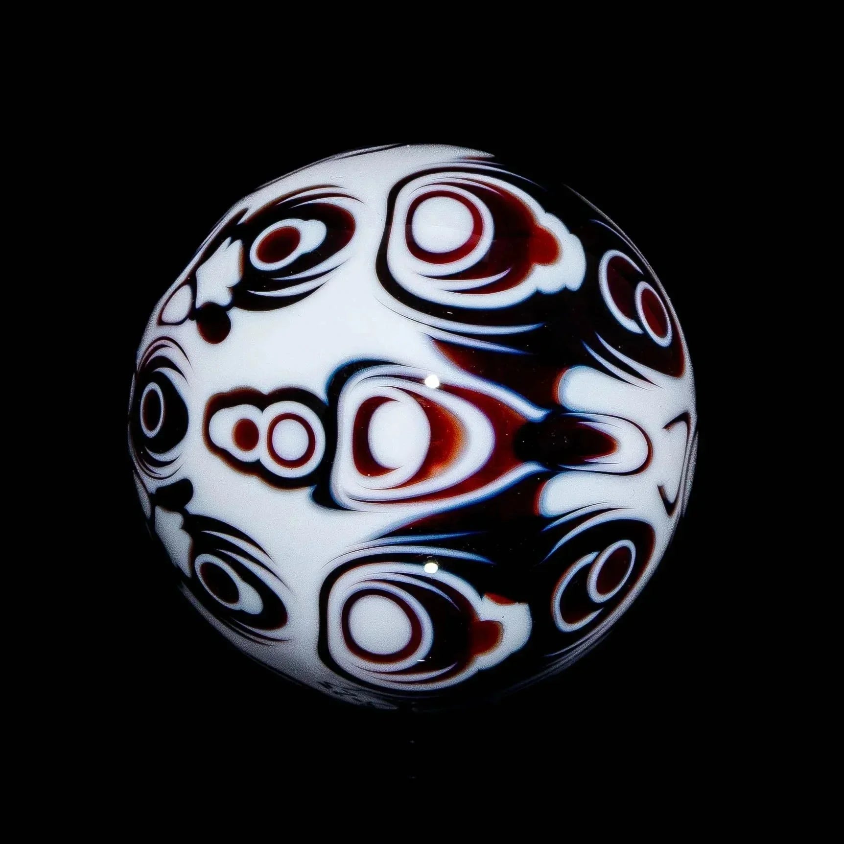 Hand-blown glass marble with intricate red and black psychedelic patterns on white.