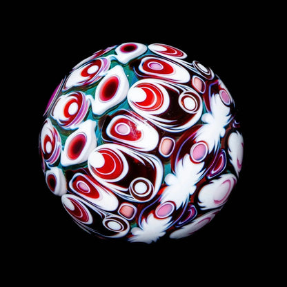 Colorful handcrafted glass marble with intricate red, white, and teal patterns on black background