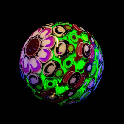 Colorful art glass marble with glowing green, purple, and red patterns on a black background