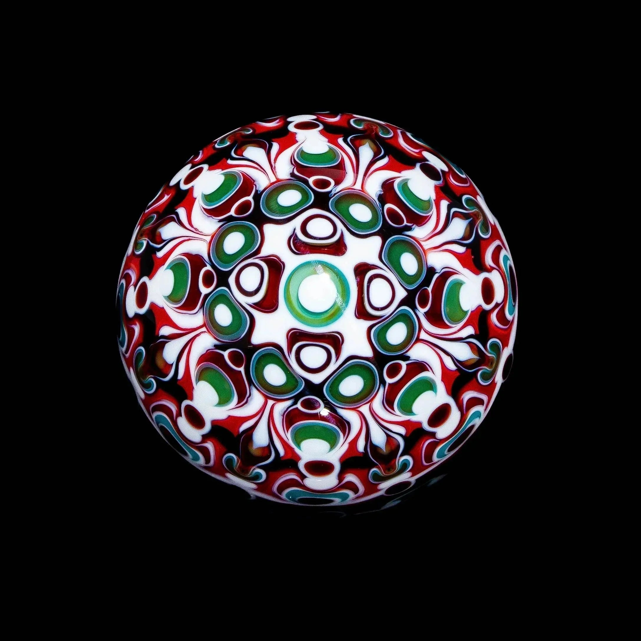 Intricate glass marble with red, green, and white abstract patterns on a black background