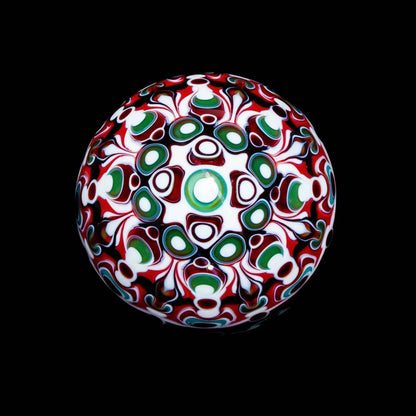 Intricate glass marble with red, green, and white abstract patterns on a black background