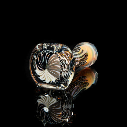 Black and white glass hand pipe with intricate swirl and cane patterns, reflected on black surface.