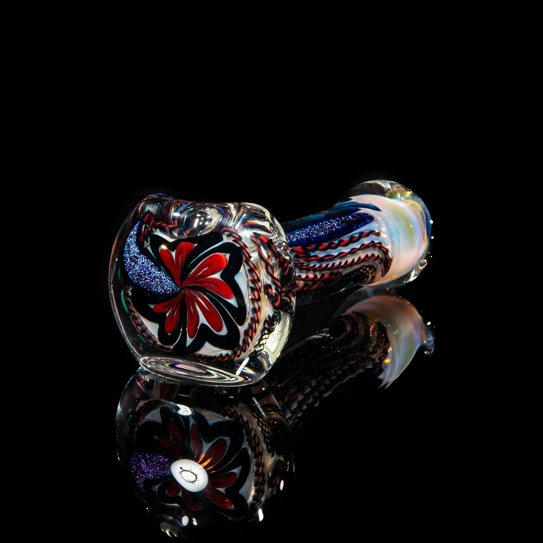 Handblown glass spoon pipe with red, blue, and white swirling patterns on black background