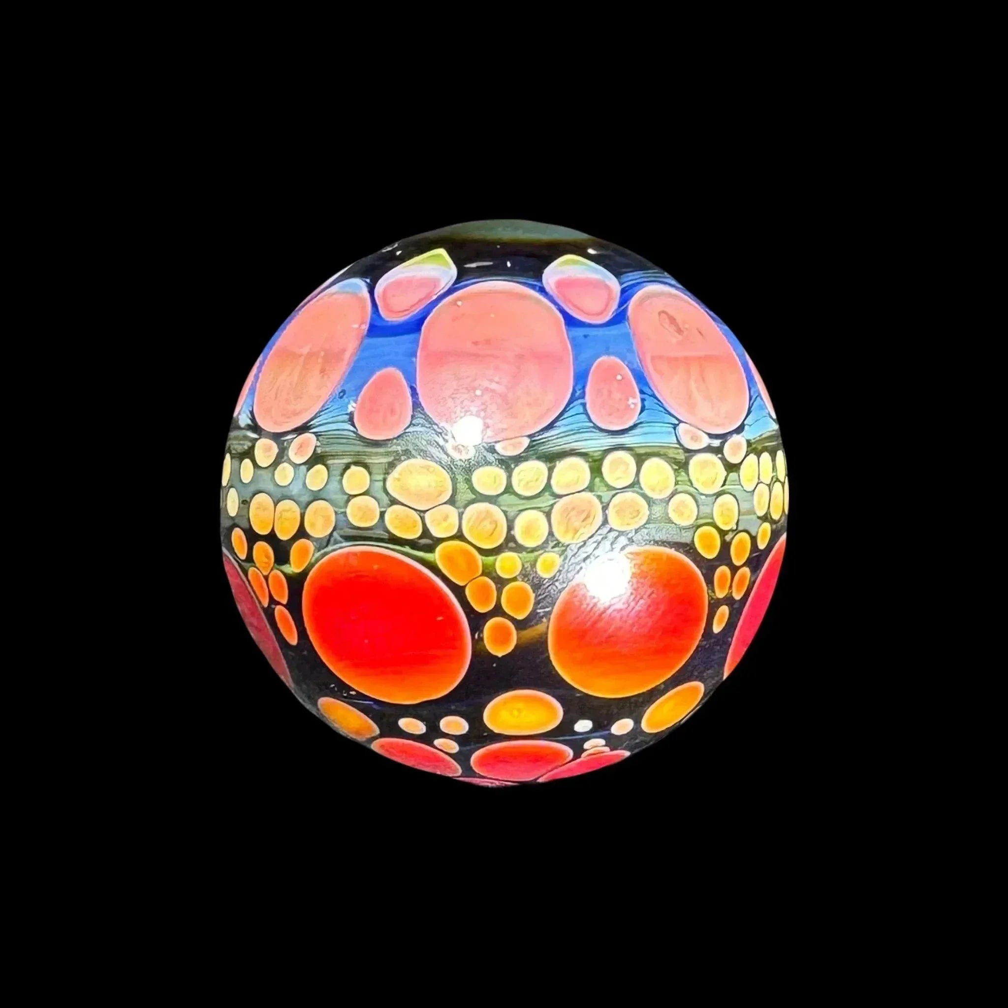Hand-blown glass marble with vibrant orange and yellow dot patterns on a black background