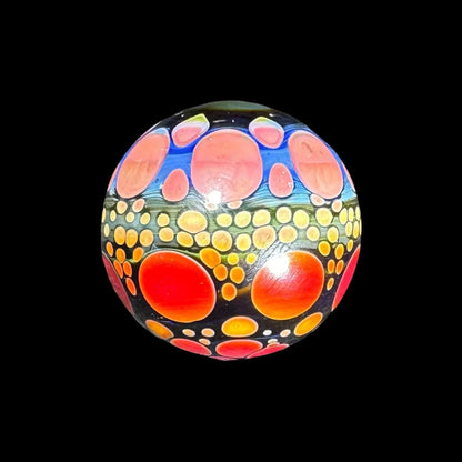 Hand-blown glass marble with vibrant orange and yellow dot patterns on a black background
