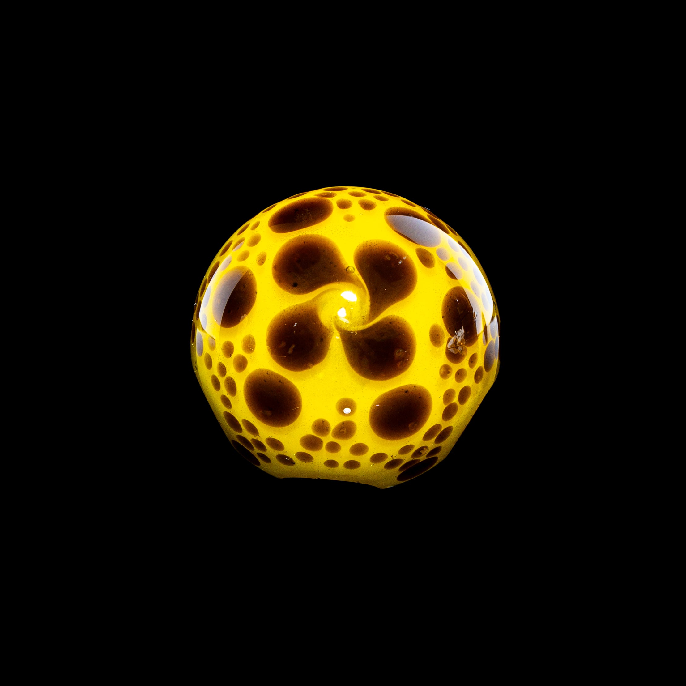Yellow glass marble with brown spots, heady glass accessory on black background