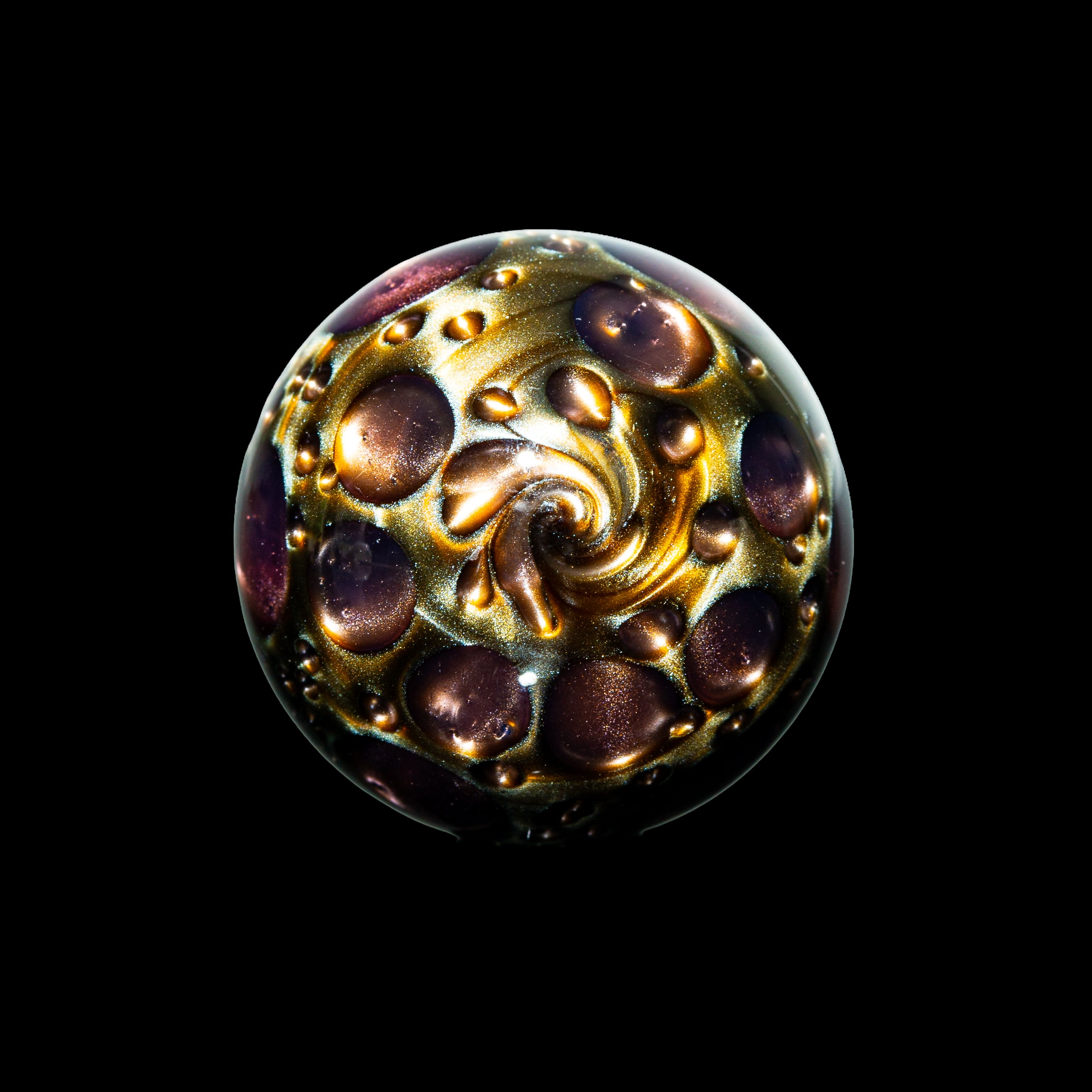 Head glass marble with gold and purple swirls and raised dots on a black background