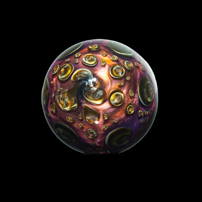 Handcrafted glass marble with metallic swirls and raised bubble details on black background