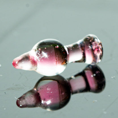 Pink glass carb cap accessory for dab rig on reflective surface
