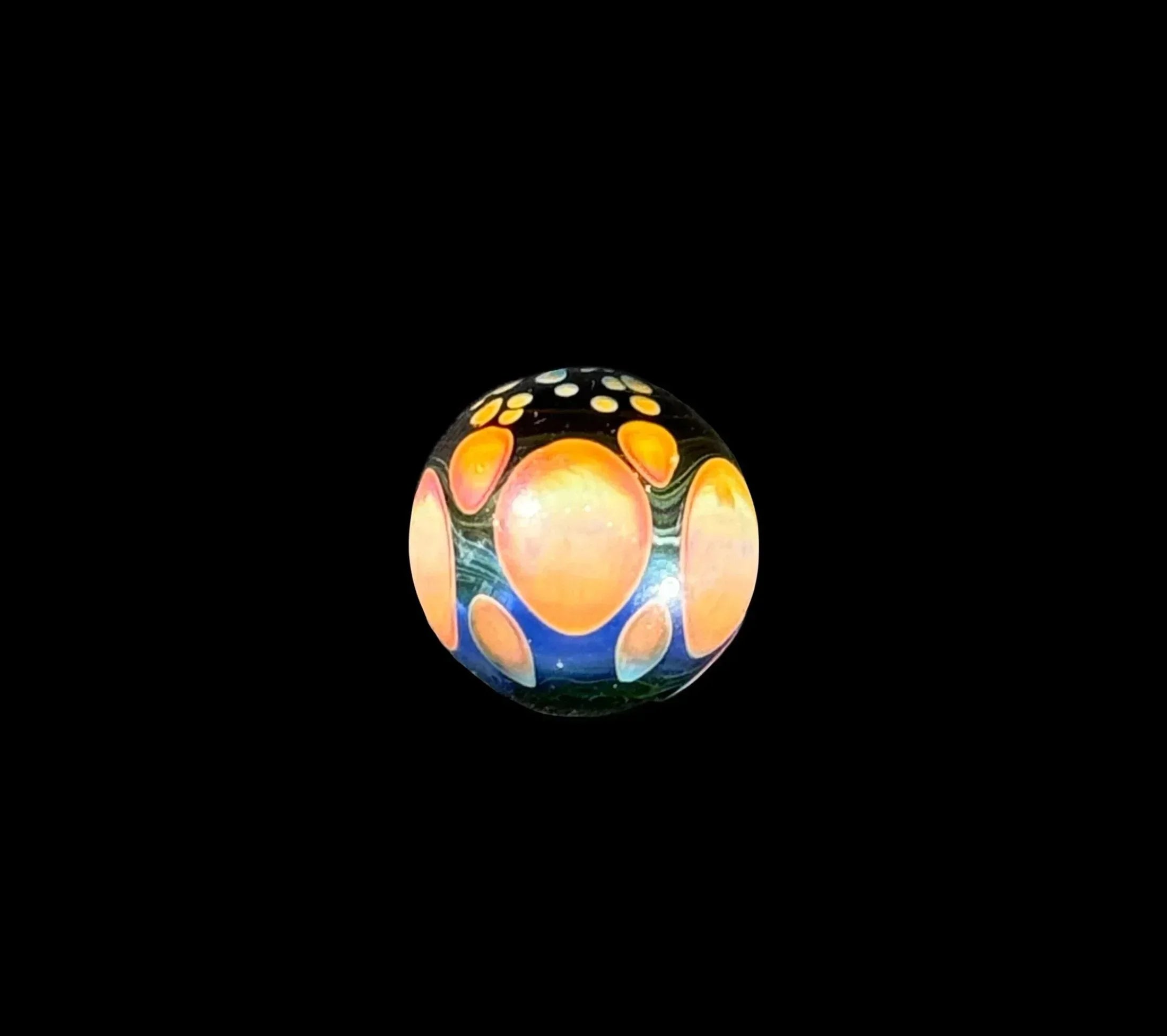 Handmade glass marble with colorful orange, blue, and yellow dot patterns on black background
