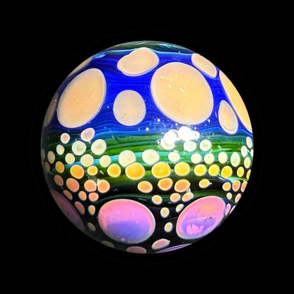 Colorful heady glass marble with blue, green, and pink dot patterns on black background