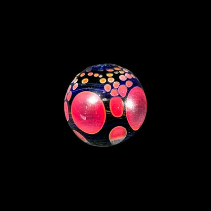 Handcrafted glass marble with red and orange dot patterns on a black background