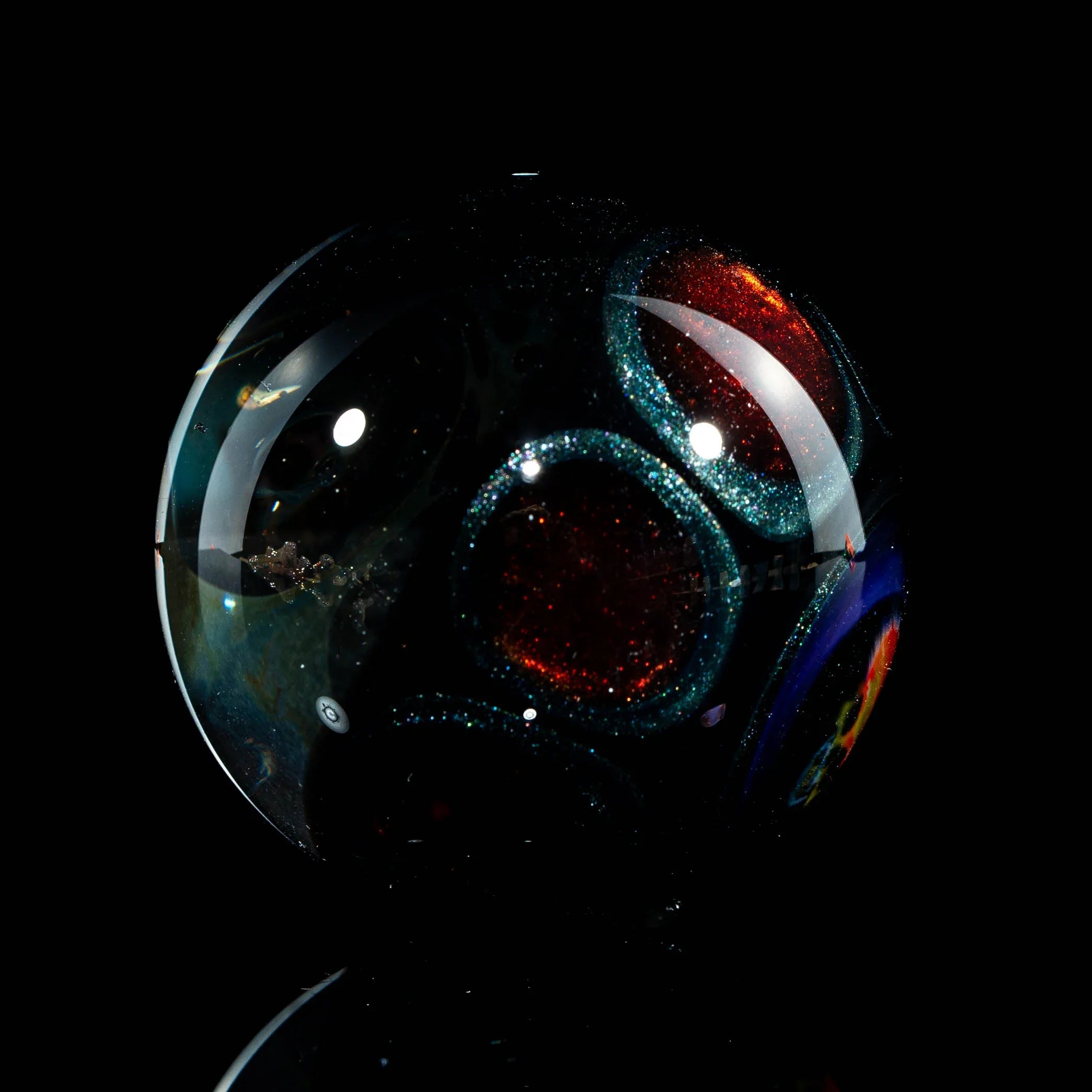 Hand-blown glass marble with shimmering red and blue circular patterns on a black background