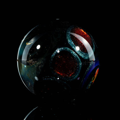 Hand-blown glass marble with shimmering red and blue circular patterns on a black background