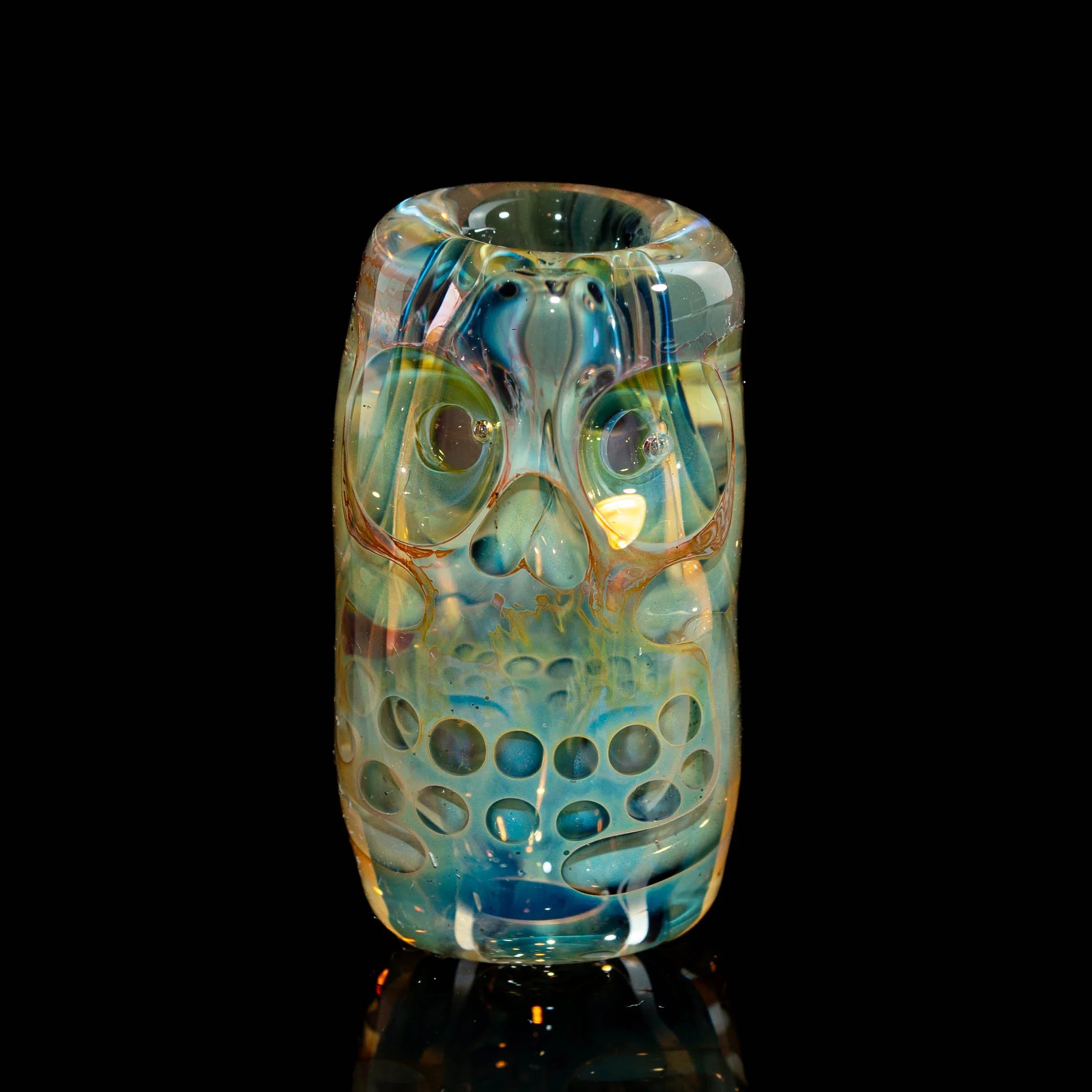 Heady glass pipe with intricate owl face design and blue-green colors on black background.