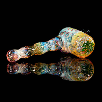Colorful heady glass pipe with intricate patterns and leaf design on black reflective surface