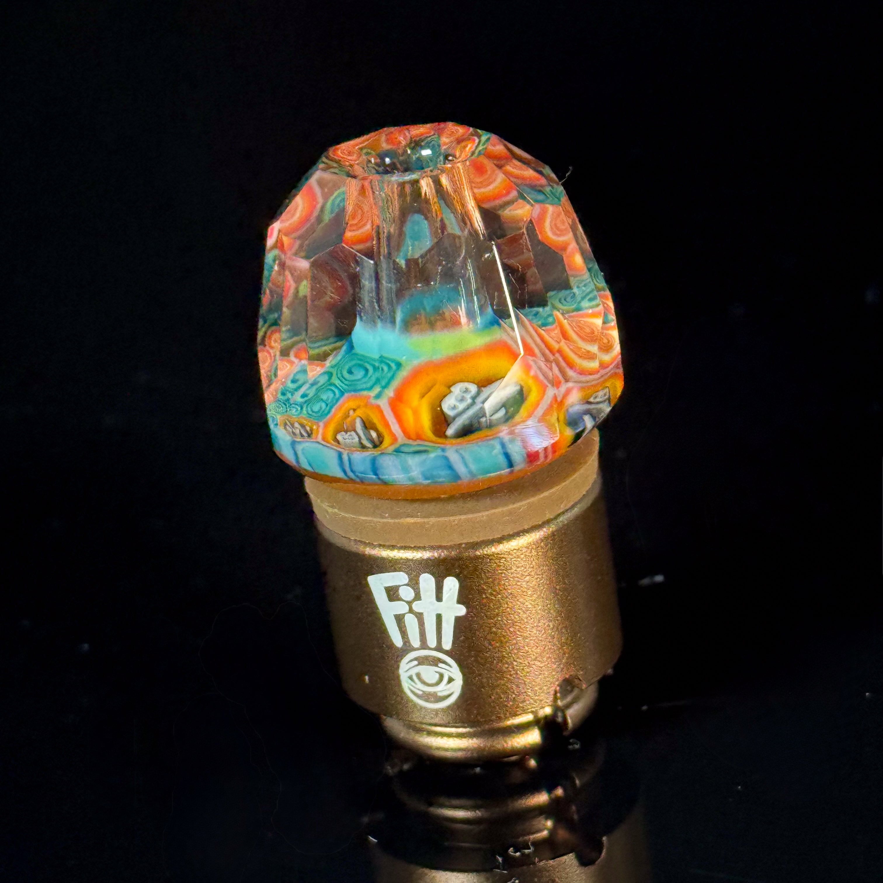 Colorful faceted glass carb cap with intricate patterns on a gold base for vaporizers.