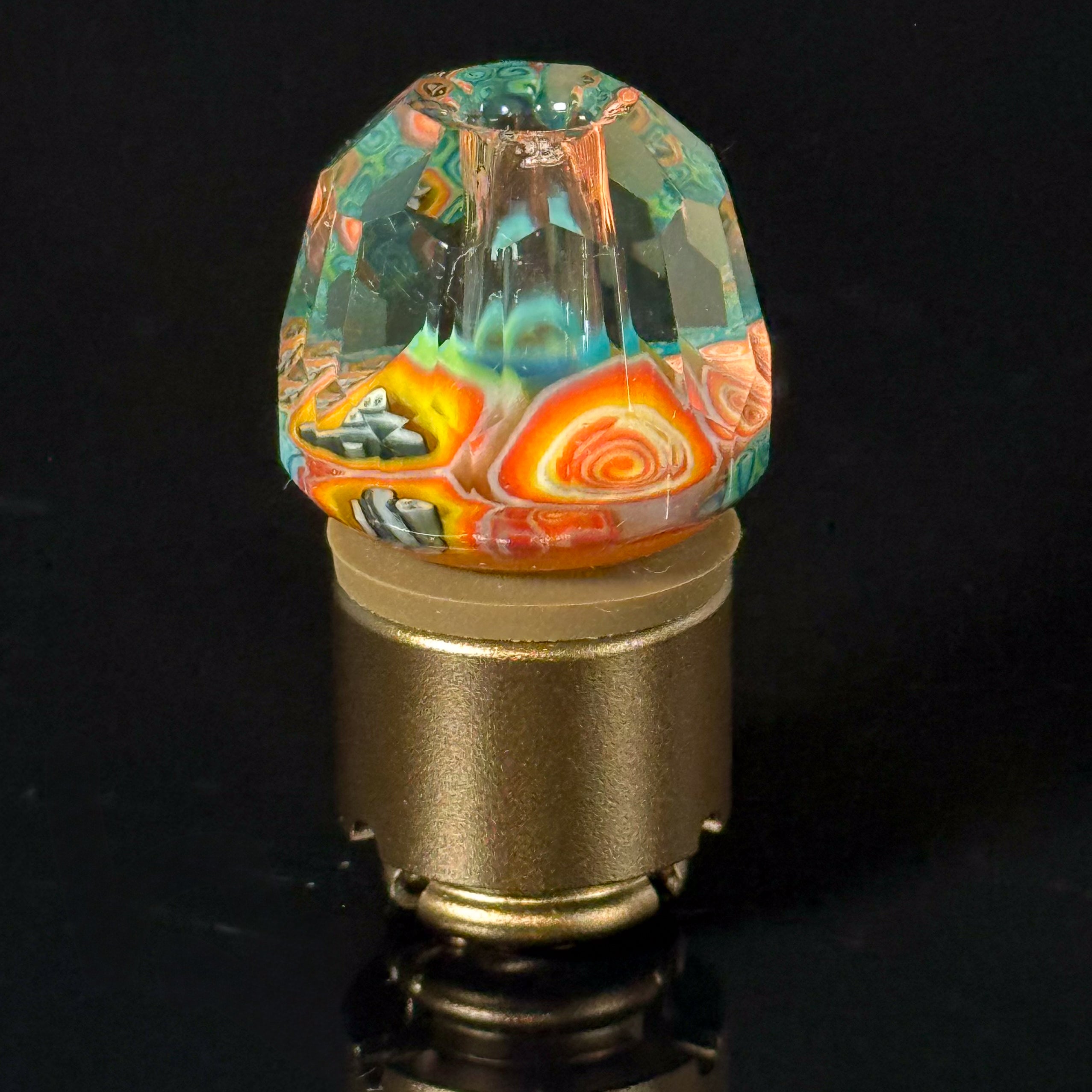 Colorful faceted glass carb cap with swirled patterns for dab rig on black background