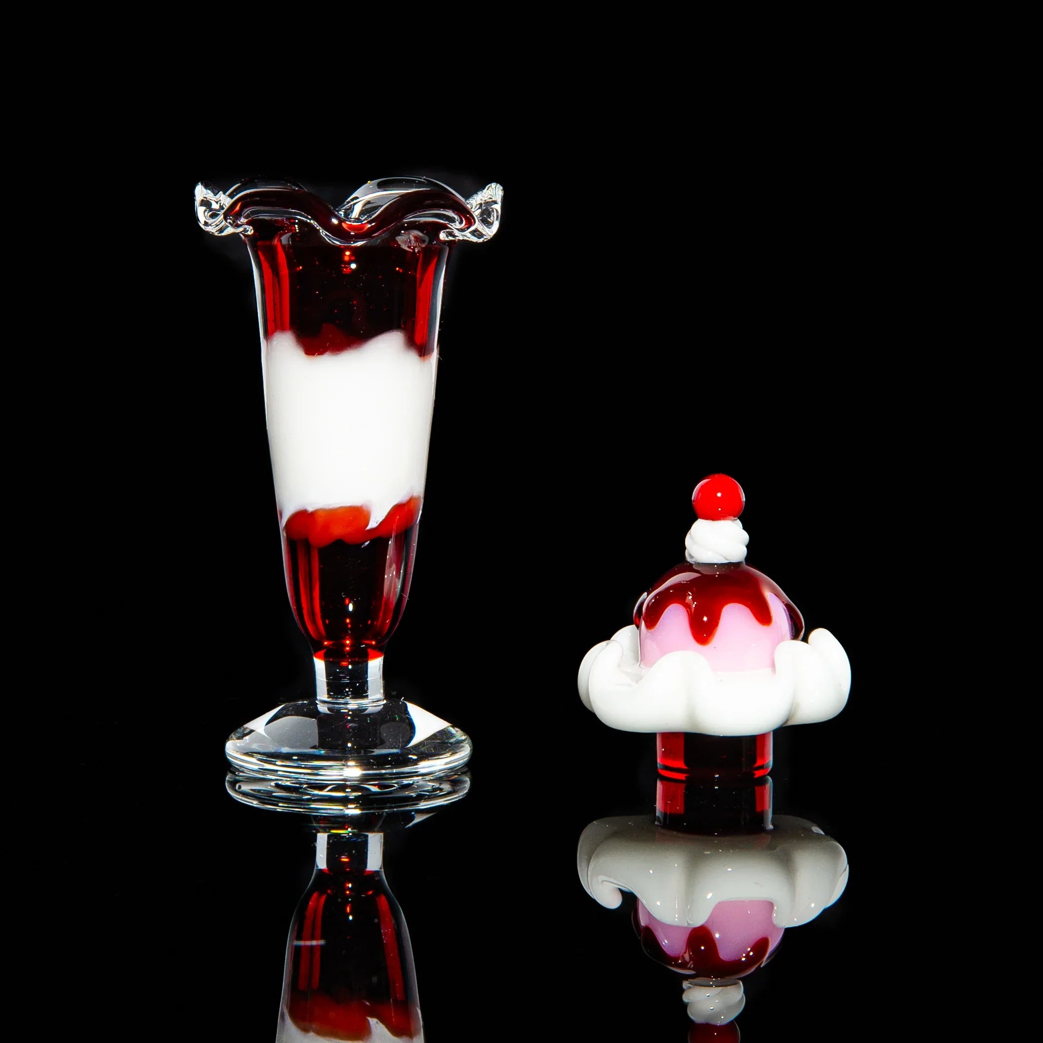 Glass sundae and parfait-shaped dab tool and carb cap set with red and white colors on black background