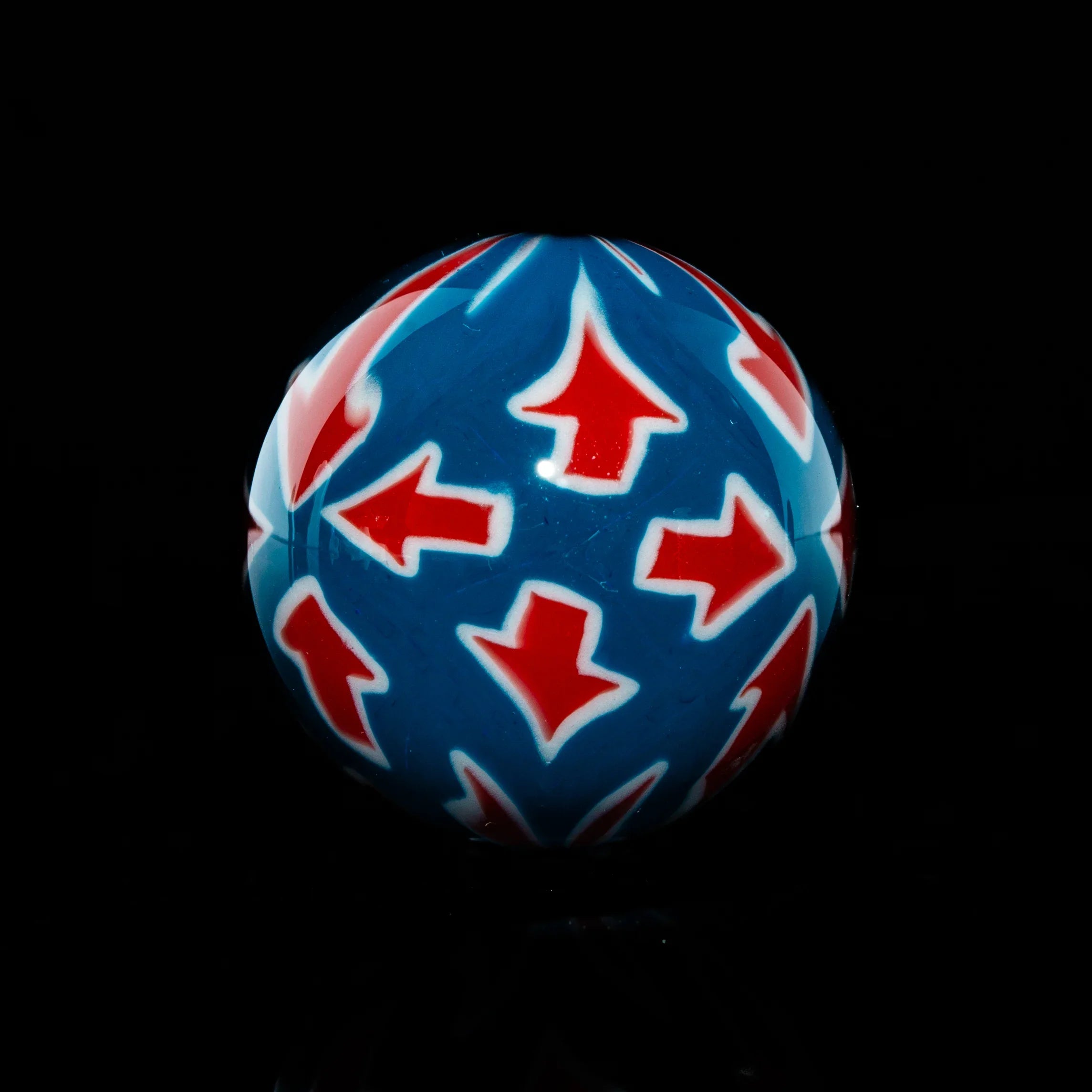 Colorful glass marble with blue base and red arrow patterns, displayed on black background.