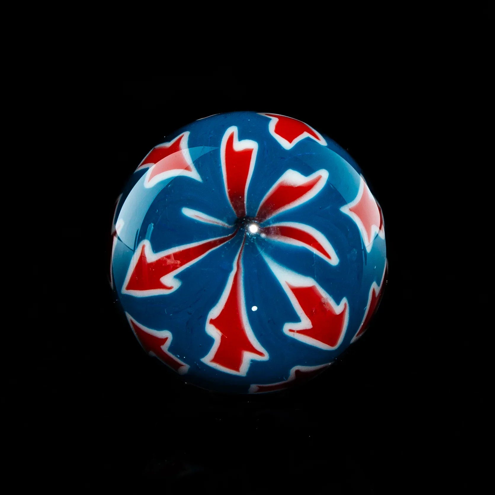 Colorful glass marble with red and white swirl design on a blue background, isolated on black