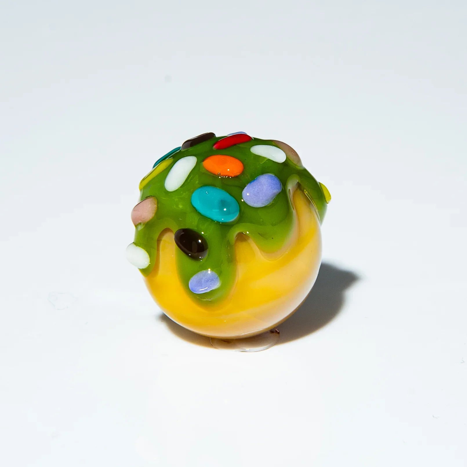 Colorful glass marble with green drizzle and rainbow sprinkles, white background