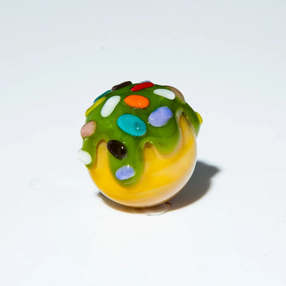 Colorful glass marble with green drizzle and rainbow sprinkles, white background