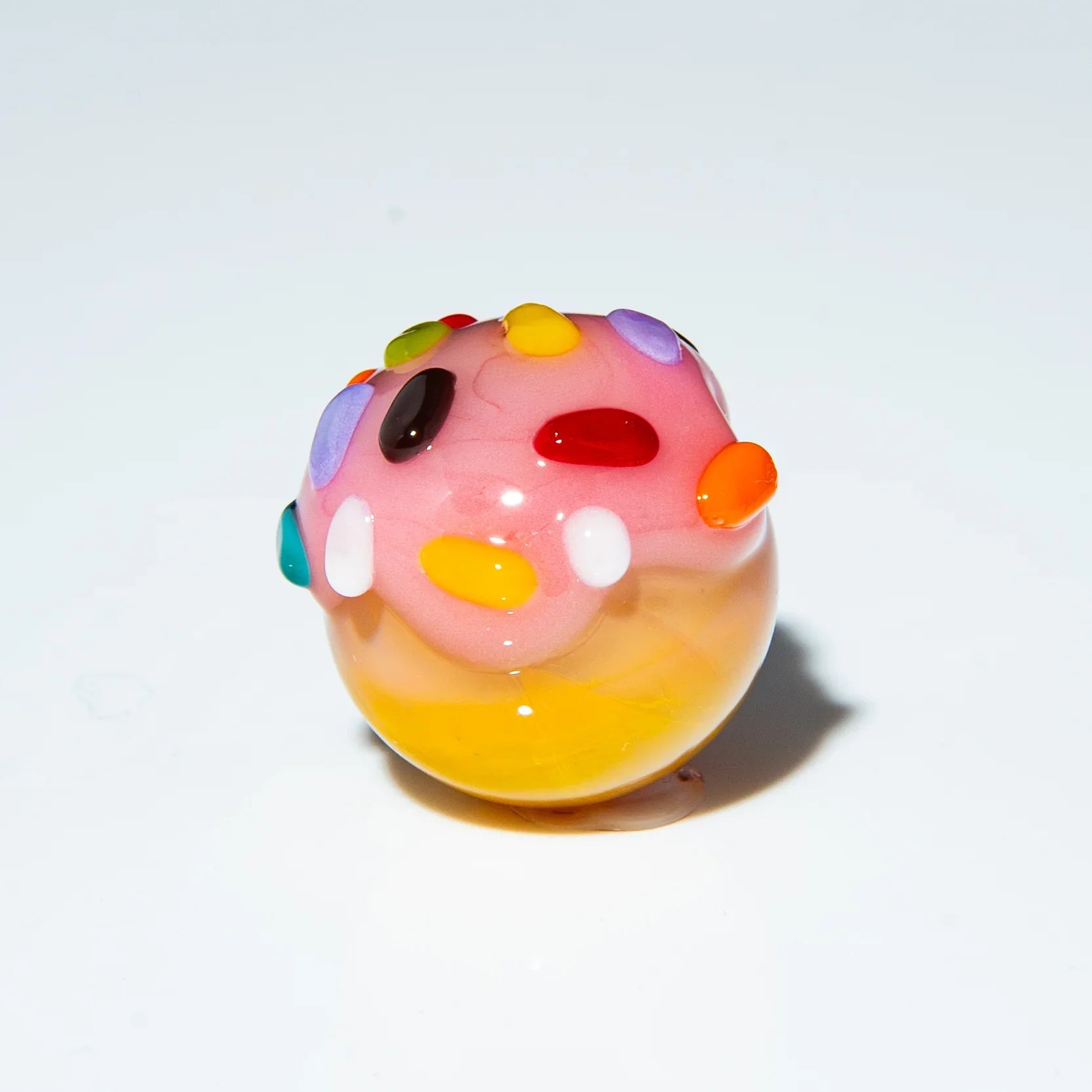Hand-blown glass marble with pink and yellow swirl, topped with colorful rainbow sprinkles.
