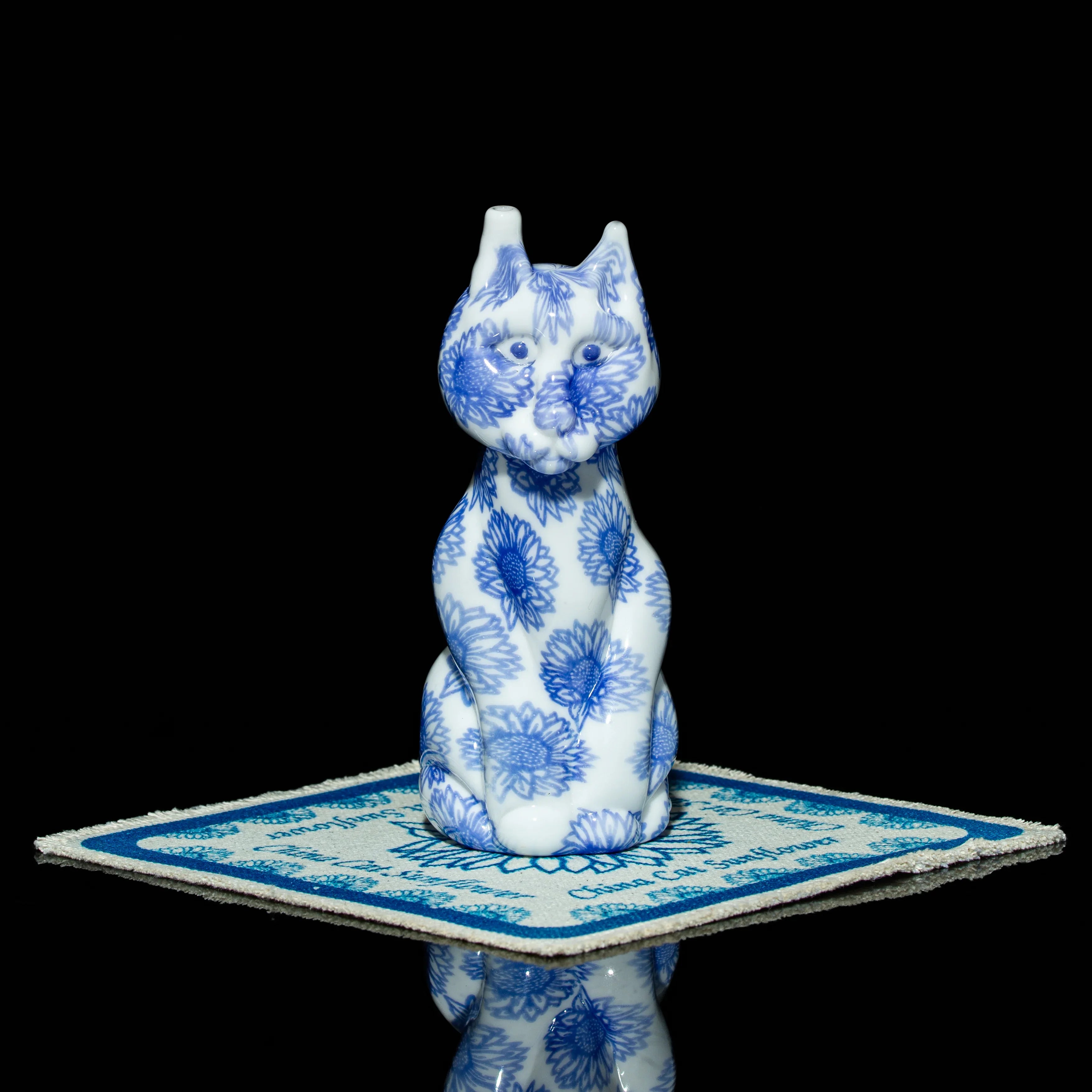 Blue and white floral glass cat figurine on a patterned coaster, black background