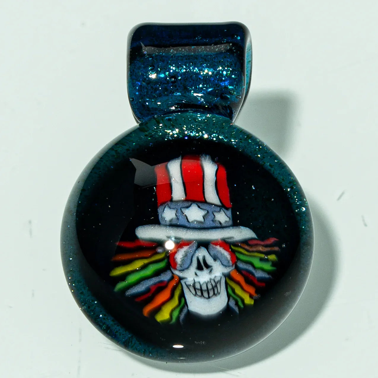 Glass pendant featuring a skull with rainbow hair and a red, white, and blue top hat