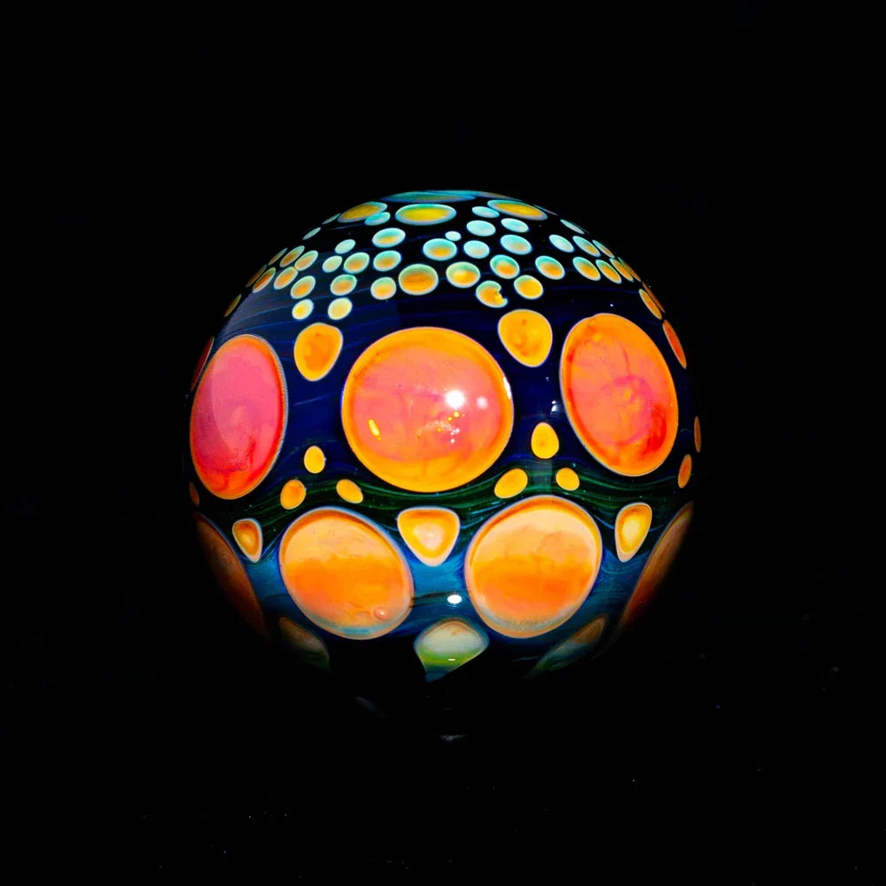 Colorful heady glass marble with orange and yellow dot patterns on a dark background.