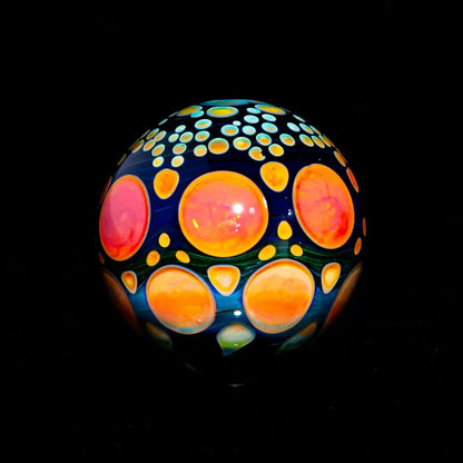 Colorful heady glass marble with orange and yellow dot patterns on a dark background.