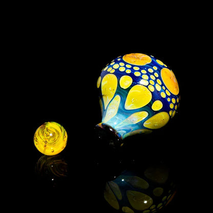 Colorful hand-blown glass carb cap and matching marble with yellow and blue patterns on black background