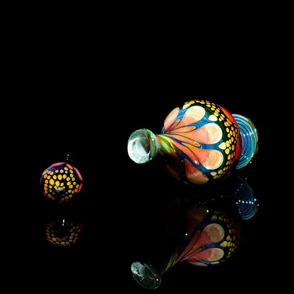 Hand-blown glass pipe with vibrant, colorful patterns and matching carb cap on black background.
