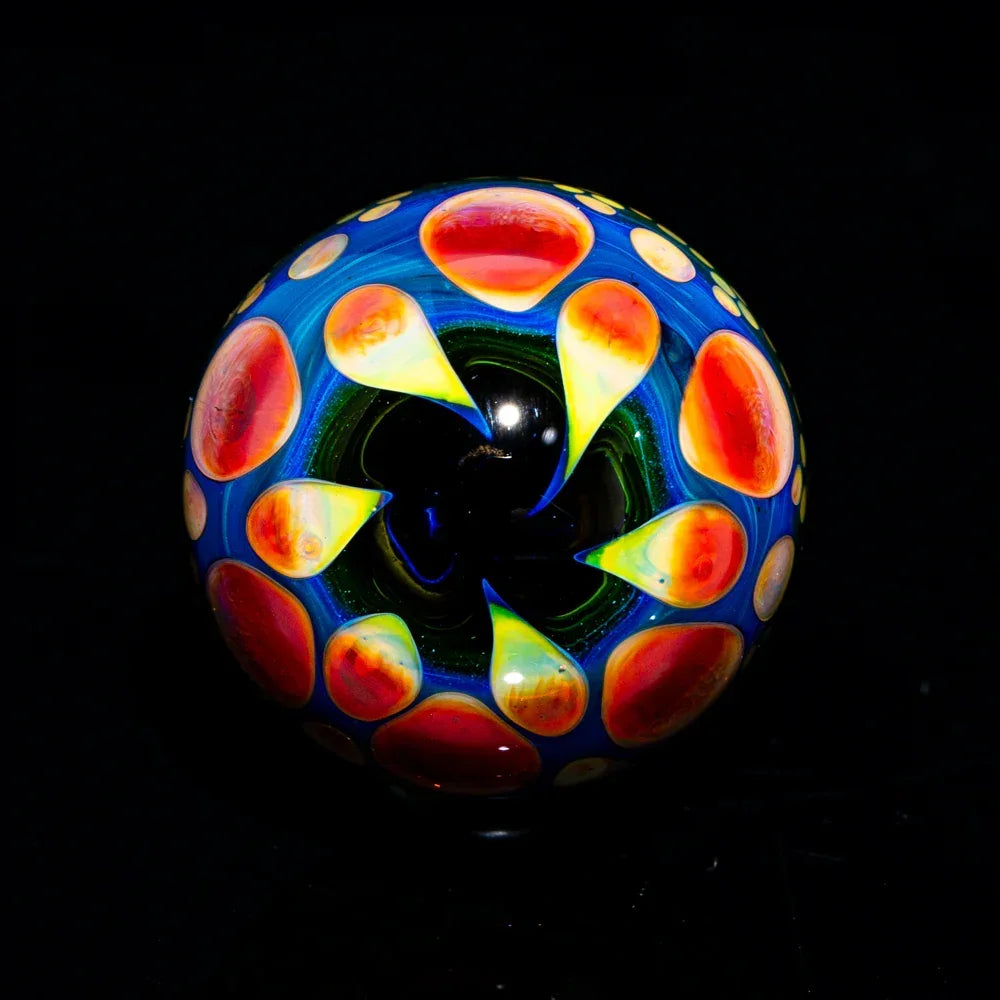 Colorful glass marble with vibrant red and yellow dots on a dark background