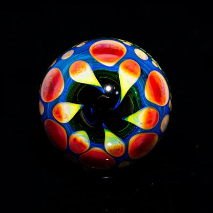 Colorful glass marble with vibrant red and yellow dots on a dark background