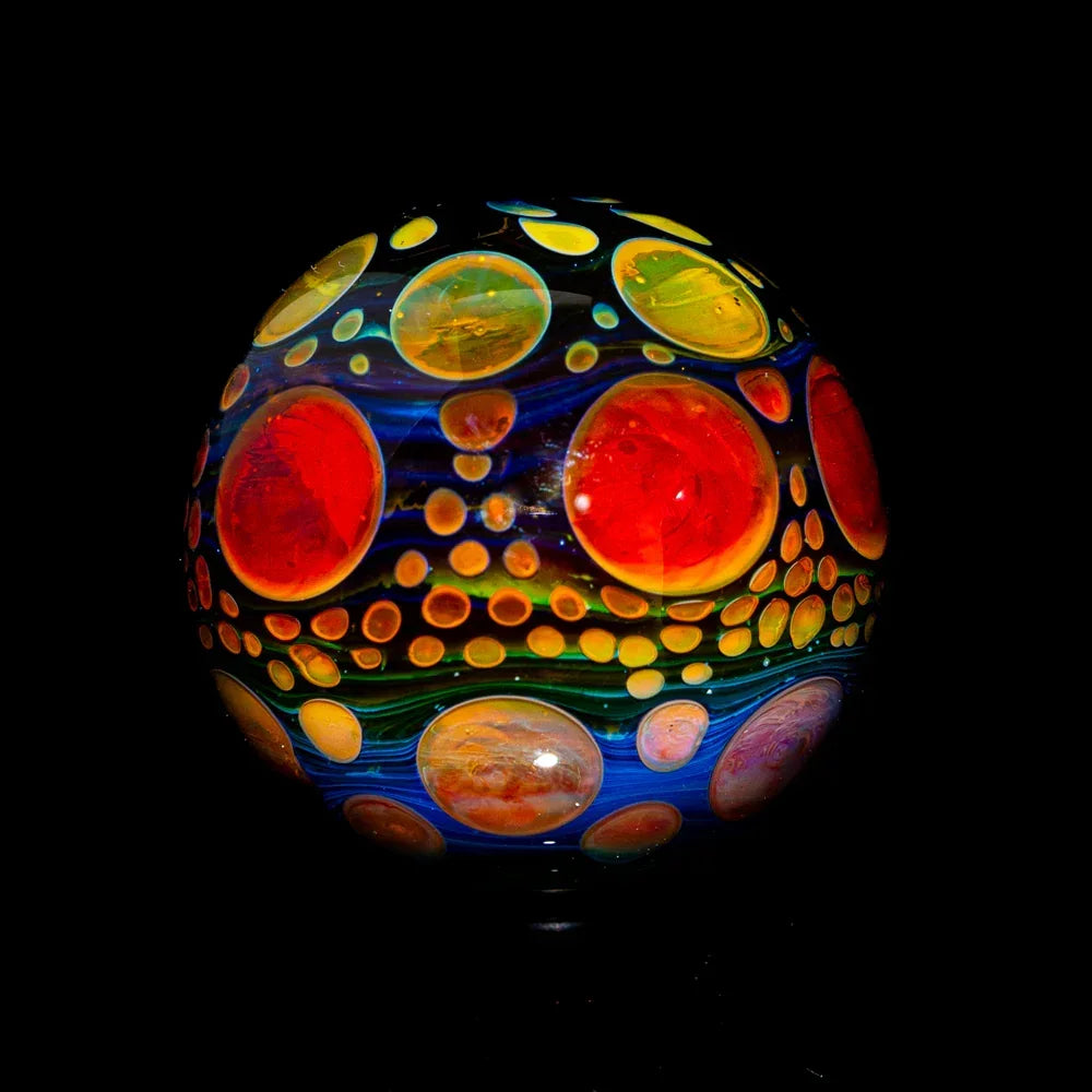 Colorful heady glass marble with vibrant red, yellow, and blue swirling patterns on black background