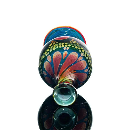 Colorful hand-blown glass jar with vibrant floral pattern, reflected on black surface.