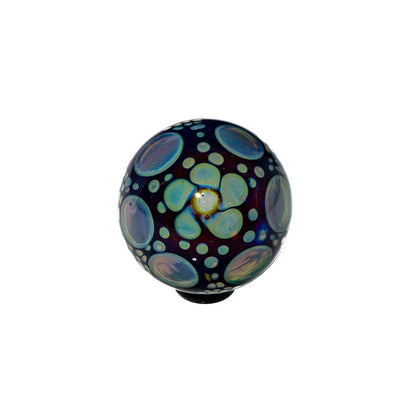Hand-blown glass marble with blue and iridescent flower petal patterns on dark background