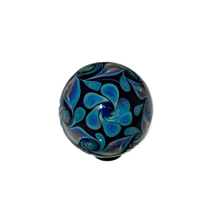 Handcrafted glass marble with blue and green swirled pattern on white background